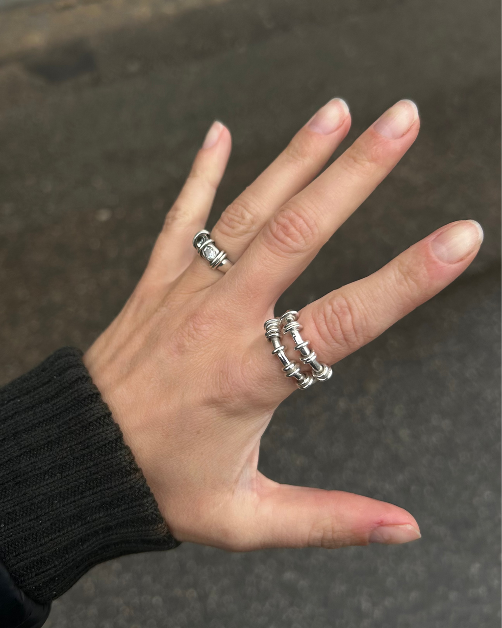 Hand wearing two silver rings on a blurred background